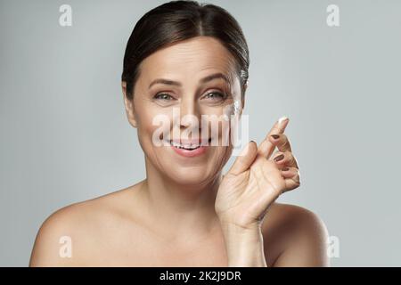 Middle aged woman applying anti-aging cream on her face Stock Photo