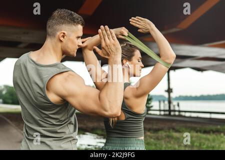 Woman during workout with a personal fitness instructor using rubber resistance bands outdoors Stock Photo