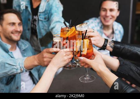 Friends celebrating and holding glasses with different alcohol drinks in a bar. Stock Photo