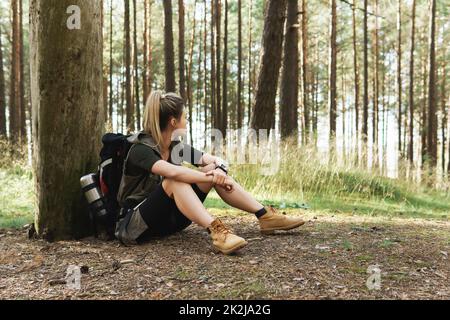 Female hiker during small halt sitting on the ground in green forest Stock Photo