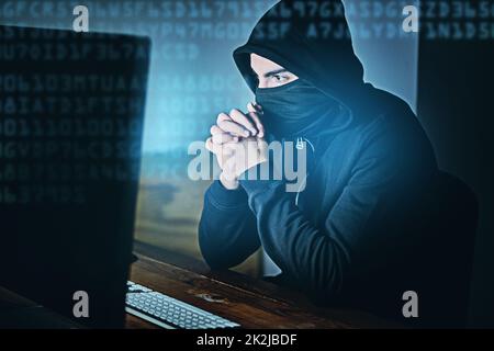 Some clicks and youre hacked. Shot of a young hacker using a computer late at night. Stock Photo