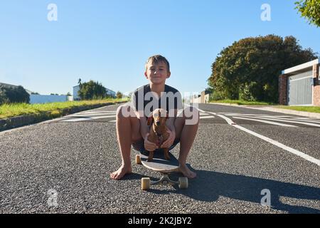 Teaching my dog has to skate. Full length portrait of a young boy and his dog sitting on a longboard. Stock Photo