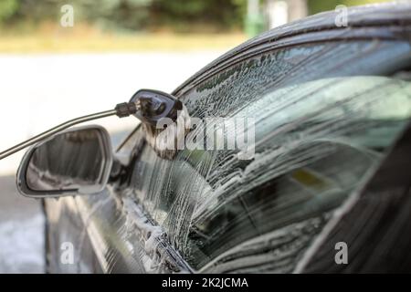 Side of a car washed in self serve carwash. Brush cleaning glass, strokes visible in shampoo foam. Stock Photo