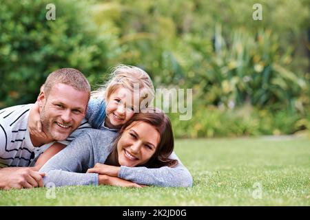 Having the best time with Mom and Dad. Portrait of a happy family of three lying outside on the grass. Stock Photo