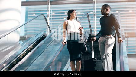 They hope to work together again in future. Cropped shot of two young businesspeople having a chat while going down an escalator in a modern workplace. Stock Photo