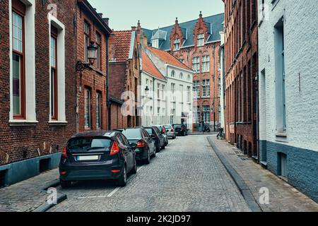 Brugge street with cobblestone road with parked cars and old medieval houses. Bruges, Belgium Stock Photo