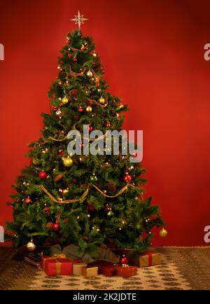 Its Christmastime. Studio shot of a decorated Christmas tree with gifts underneath it. Stock Photo