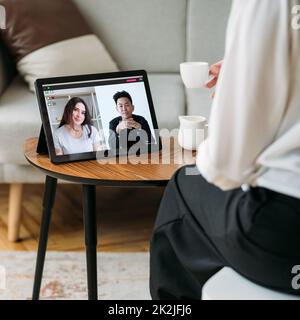 Home web chat. Online coffee break. Virtual communication. Distance talk. Diverse people meeting on tablet screen at modern interior. Stock Photo
