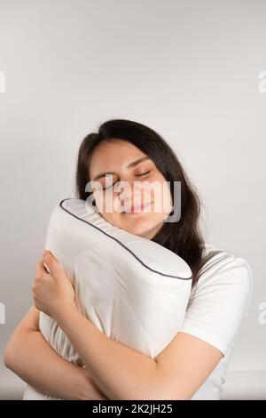 A woman hugs an orthopedic pillow made of memory foam on a white background. Choosing pillows for healthy sleep. Stock Photo