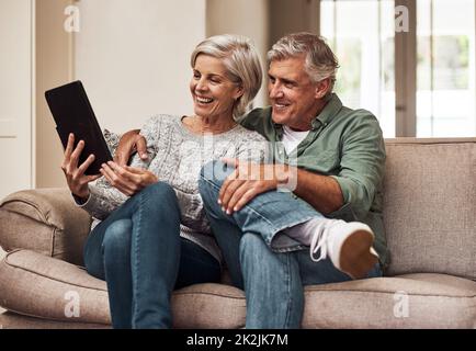 We dont know a television anymore. Cropped shot of a cheerful senior couple browsing on a digital tablet together while being seated on a couch at home during the day. Stock Photo