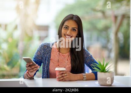 I come for the wifi, but the coffees good too. Portrait of an attractive young woman using her cellphone while drinking coffee in a coffee shop. Stock Photo