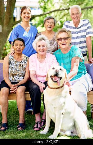 Their autumn years are filled with happiness. Portrait of a group of smiling seniors and a nurse outside with a labrador. Stock Photo