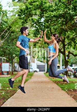 That workout was so worth it. Shot of a sporty young couple high fiving in mid-air while exercising outdoors. Stock Photo