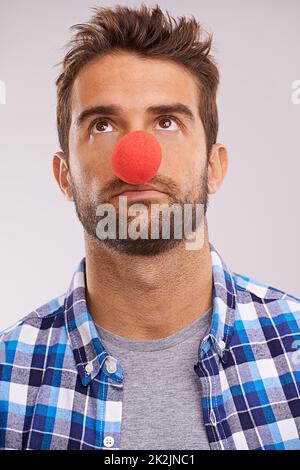 Clowning around. Studio shot of a handsome man wearing a red nose against a gray background. Stock Photo