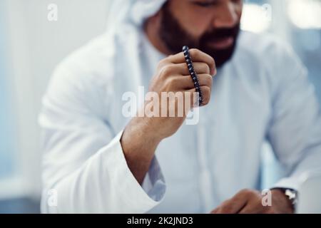 Seeking divine intervention. Cropped shot of a young businessman dressed in Islamic traditional clothing holding prayer beads while working in his office. Stock Photo