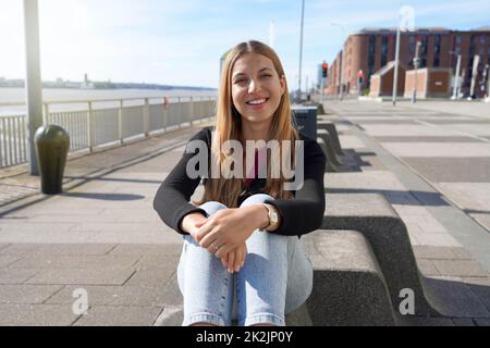 Young beautiful woman sitting relaxed on Liverpool waterfront on sunny day, England Stock Photo