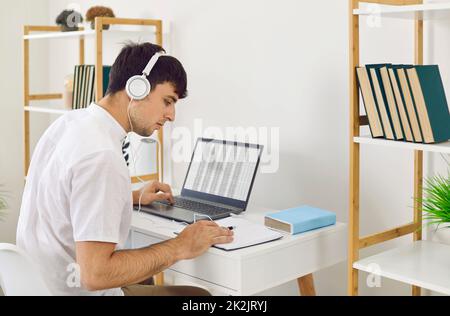 Young man enjoying music in headphones and working or studying on laptop in home office. Stock Photo
