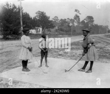 Three African American children playing golf with clubs made of sticks.   c1905. Stock Photo