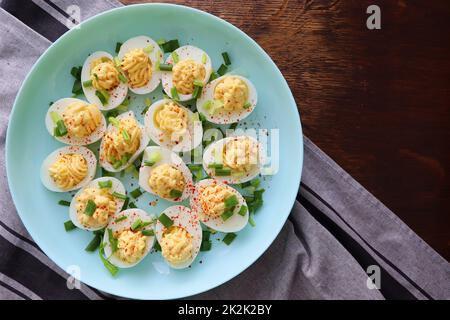Deviled Eggs sprinkled with paprika and chopped green onion on a green plate on a woodene table . Top view Stock Photo
