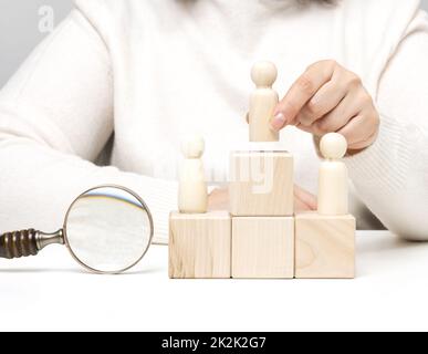 a woman in a white sweater puts a wooden figurine on the podium. The concept of employee search, career advancement. Talented employee Stock Photo