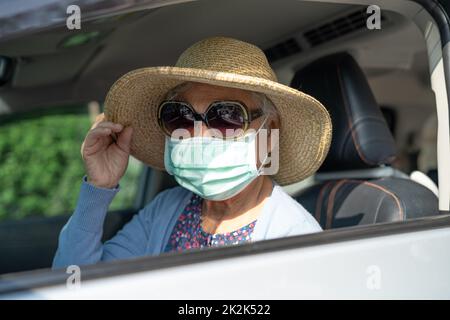 Asian elderly woman with mask and hat sitting in car with enjoy and freedom in traveling trip. Stock Photo