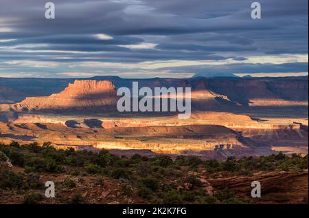 Spotlighting on Ekker Butte & Green River Basin, viewed from the Candlestick Tower Overlook, Canyonlands NP, Utah.  Orange Cliffs & Henry Mountains be Stock Photo