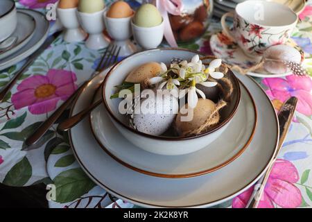 Stylish Easter table setting with egg in bowl on table. Modern natural dyed easter egg, flowers on plate and cutlery. Easter festive table decorations Stock Photo