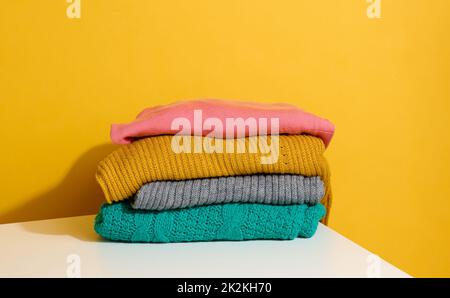 stack of folded knitted sweaters on yellow background. Comfortable clothes, wash Stock Photo