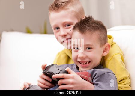 Two young brothers playing video games together on a sofa Stock Photo