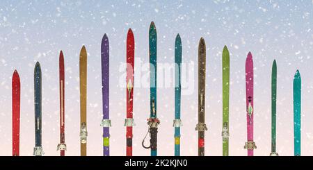 Row of vintage weathered skis in front of a blue sky with snowfall Stock Photo