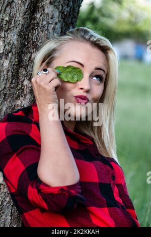 Playful young woman covering her eye with a green leaf Stock Photo
