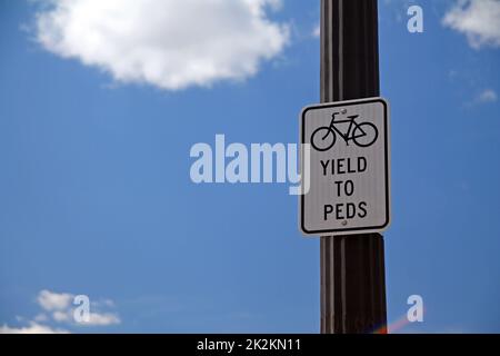 Yield to Peds sign hanging on a black pole with bicycle icon Stock Photo
