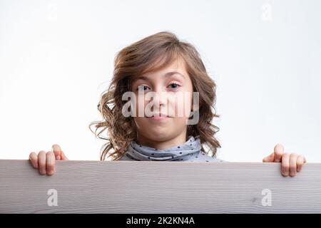 Young girl looking over the top of a wooden board with a smile Stock Photo