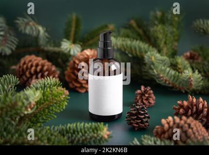 Brown glass dispenser near fir branches and pine cones on dark green close up. Brand packaging mockup. Stock Photo