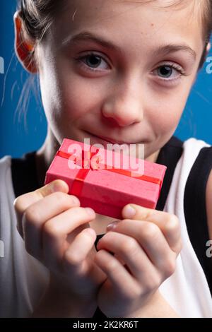 Little girl with big blue eyes holding up a small red gift box Stock Photo