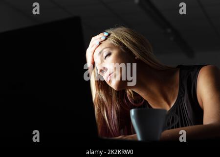 Exhausted businesswoman working overtime in a dark office Stock Photo