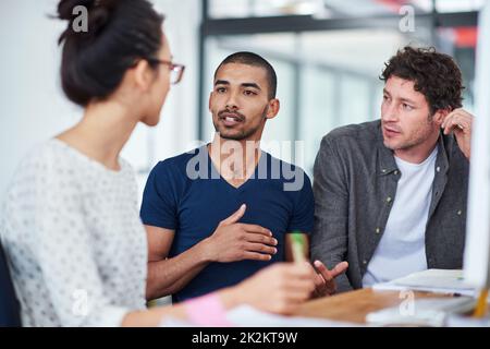 Getting creative with colleagues. a group of designers talking together while sitting at their workstations in an office. Stock Photo