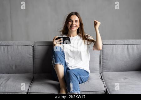 Happy excited smartphone user shouting for joy, getting good news, reading text message on cellphone screen, making winner yes hand gesture. Surprised Stock Photo