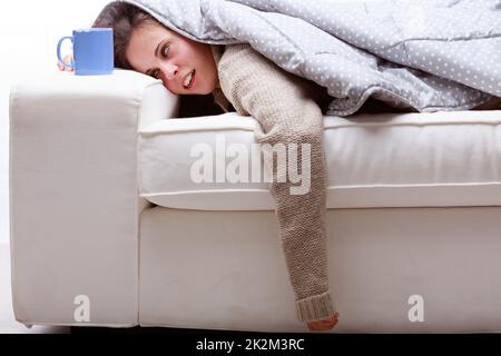 Young woman covered in a duvet passed out on a sofa Stock Photo