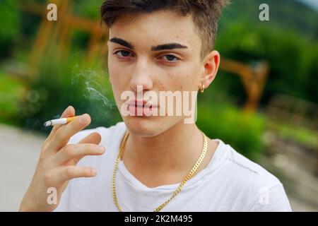 Serious young man smoking a cigarette outdoors exhaling the smoke Stock Photo