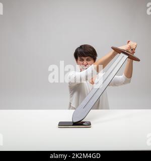 Angry woman attacking her mobile with a sword Stock Photo