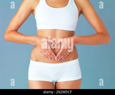 For the greatest wealth, invest in your health. Cropped studio shot of a fit young woman making a heart shaped gesture over her stomach against a blue background. Stock Photo