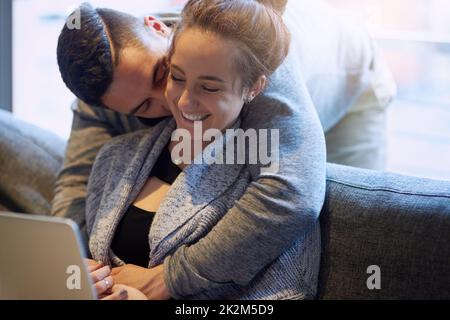Showering her with affection. Shot of an affectionate young couple surfing the net while relaxing on the sofa at home. Stock Photo