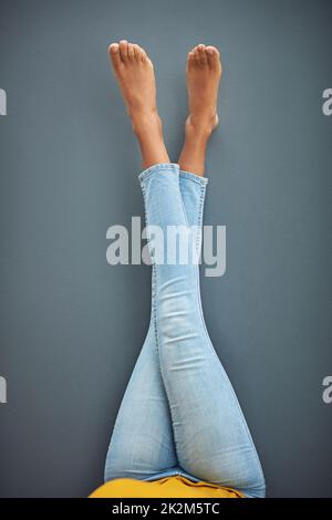 Not a care in the world. Shot of a womans crossed legs leaning against a gray wall. Stock Photo