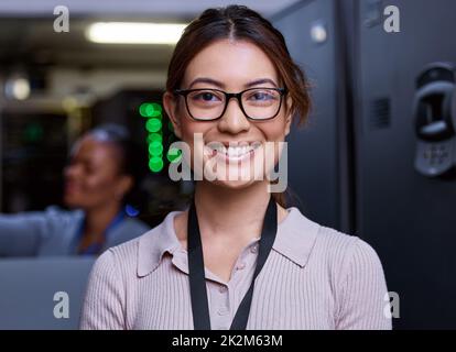 Trust me, your severs are in good hands. Cropped portrait of an attractive young female programmer working in a server room with her colleague in the background. Stock Photo