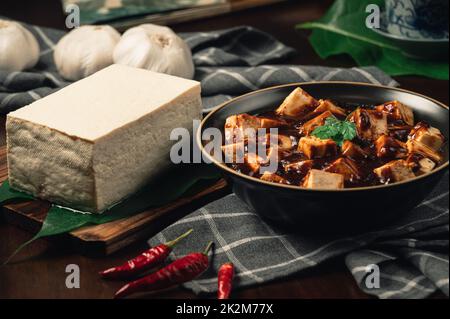 Traditional spicy hot chinese food,Mapo Tofu dressed with tea cup,on wooden plate with dark background. Stock Photo