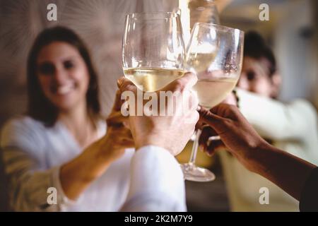 Cheerful group of people having fun toasting and drinking white wine sitting at restaurant table - friends raising glasses for a celebratory toast - f Stock Photo