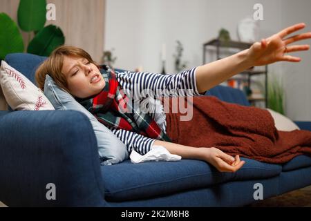 Depressed woman sick for flu or viral disease lying on sofa and asking for help Stock Photo