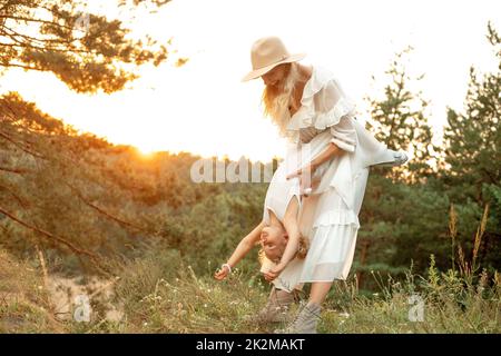 Portrait of laughing family walking in park forest, young woman mother holding upside down little girl daughter playing. Stock Photo