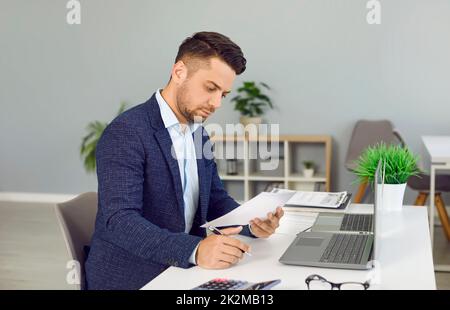 Young man reading some business documents while sitting at his desk in the office Stock Photo